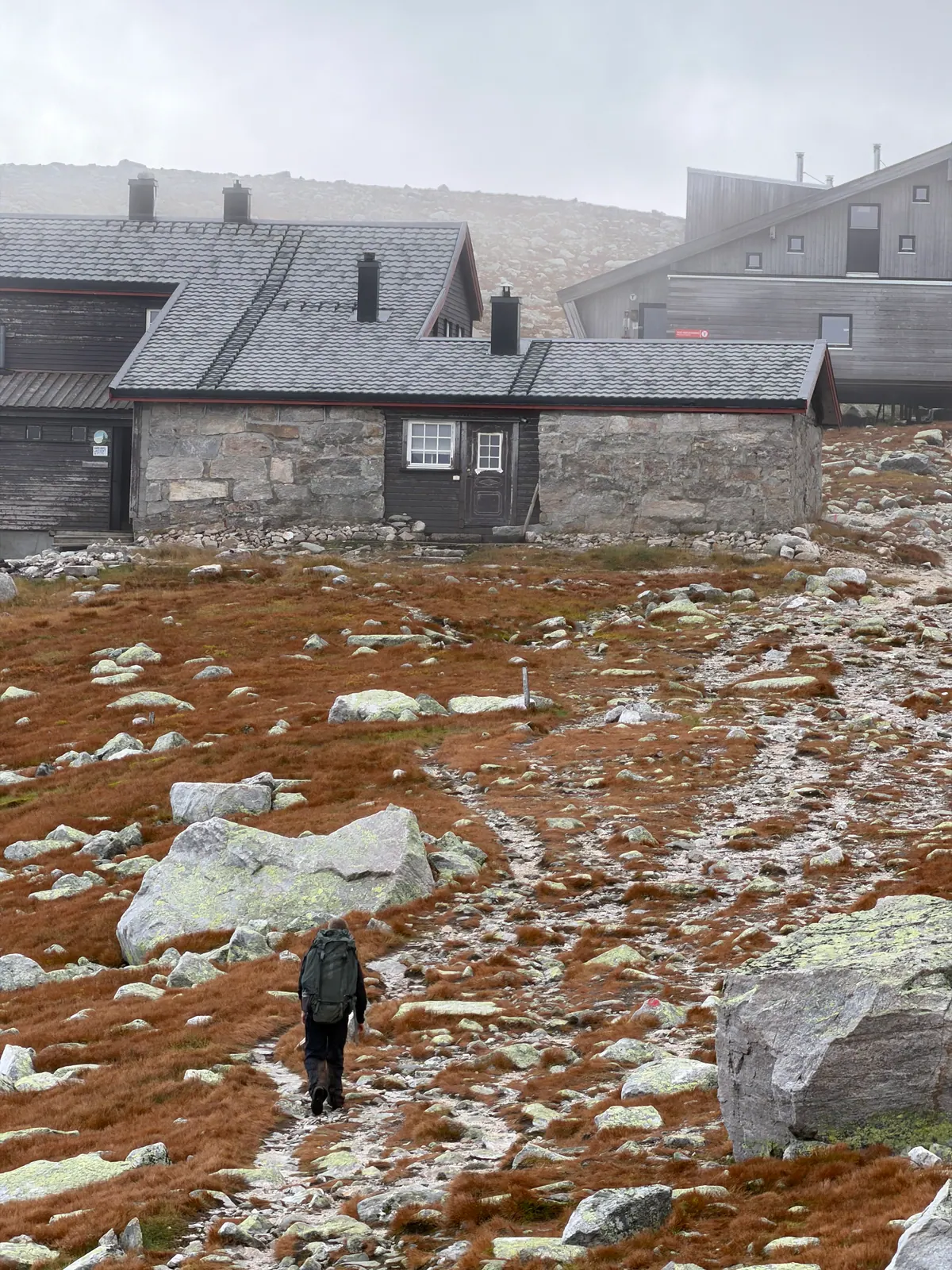 Bærer på vei mot fjellhytter med sekk i steinete terreng